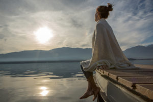 Young woman relaxes on lake pier, watches sunset. Beautiful 